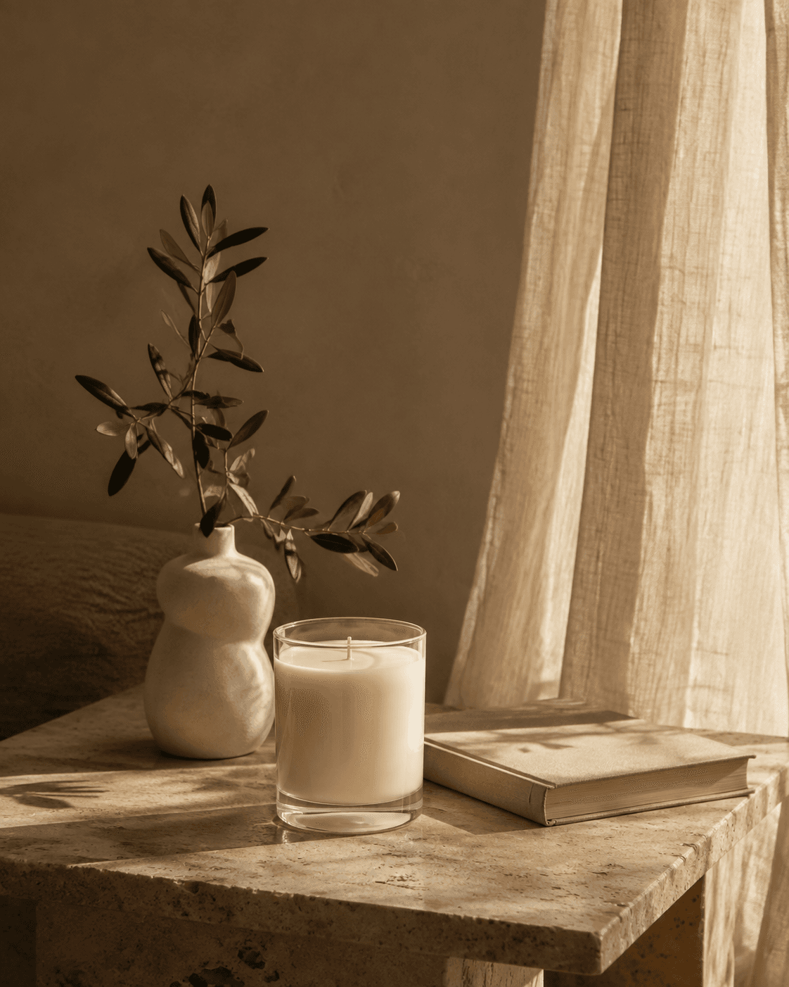 A candle glowing beside linen and an olive branch